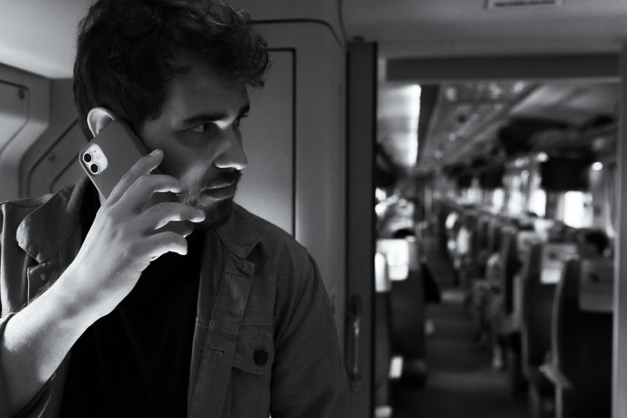 Black and white photo of a man using a smartphone while traveling on a modern train. — El mercado nocturno de Peru: puestos mapeados, platos imprescindibles traducidos.