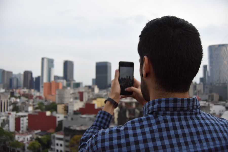 Man photographing urban cityscape with smartphone against skyline.