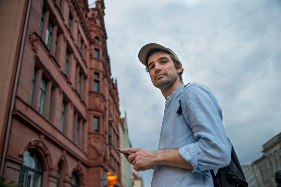 Casually dressed man using smartphone in Berlin city street with historic architecture.