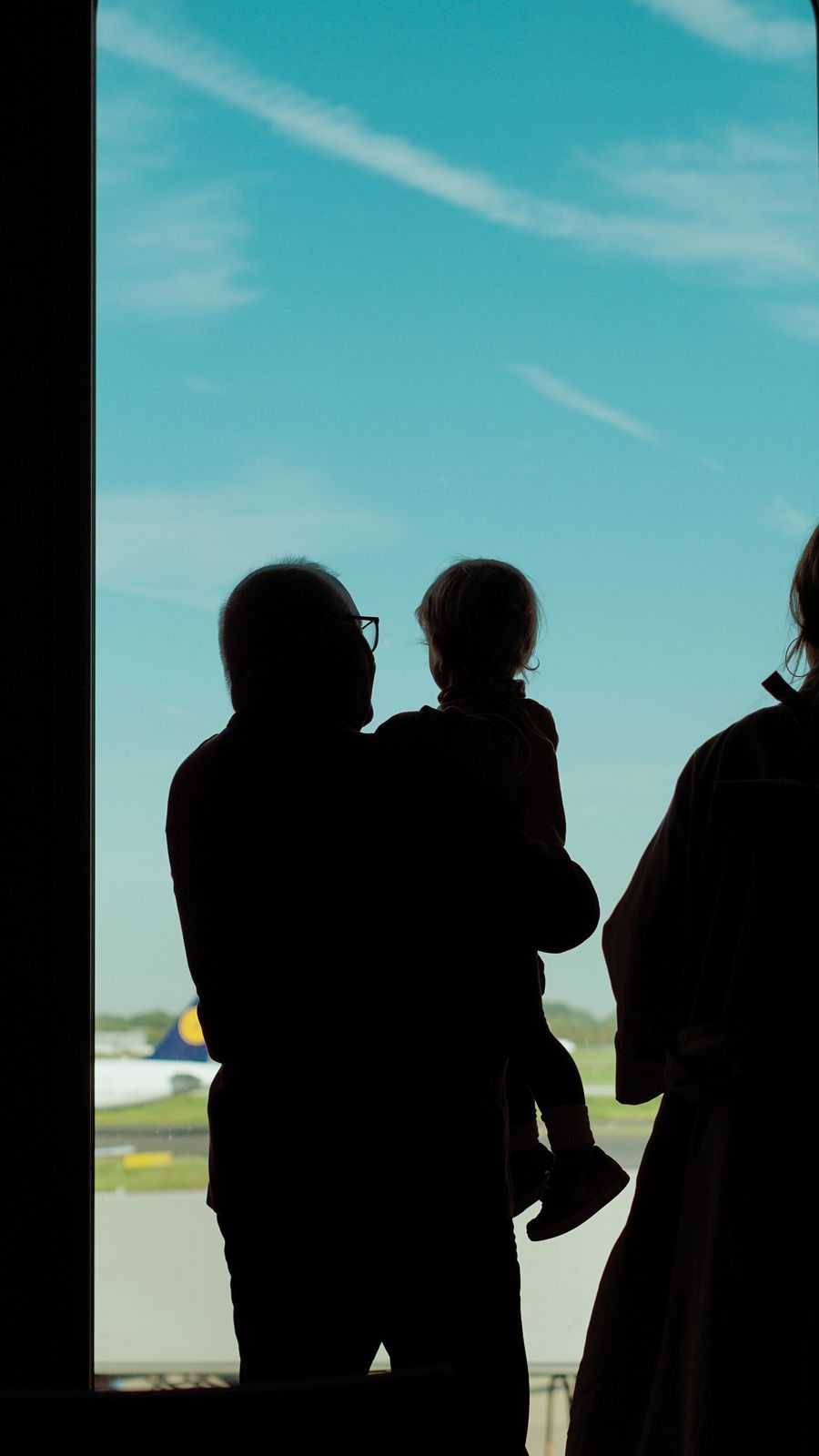 a family is silhouetted against an airport window — Día de salida en Equatorial Guinea: salida tardía solicitada, taxi sincronizado con el vuelo.