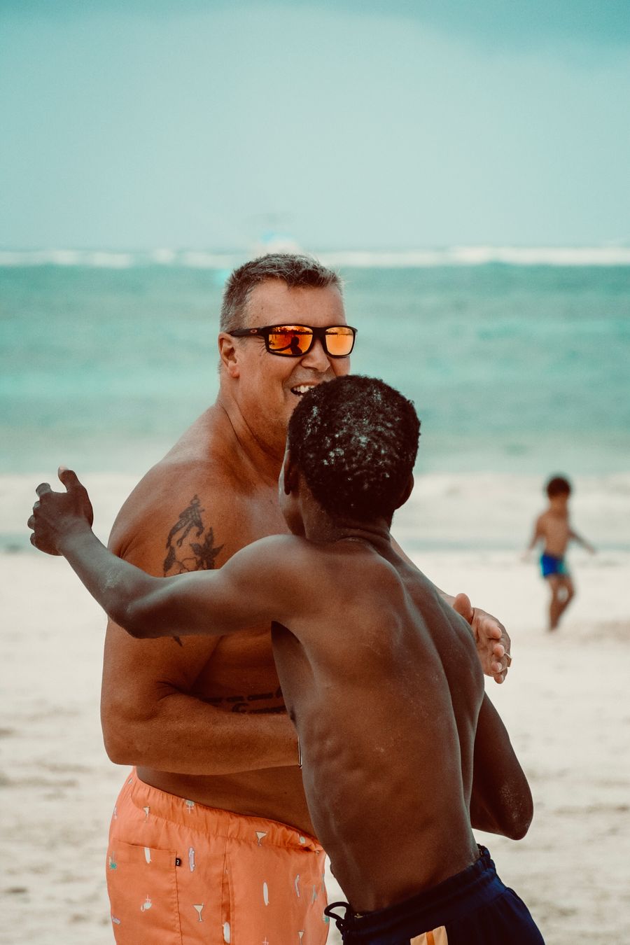a man in sunglasses and a shirt is standing on the beach with another man — Docs: Perdido en la medina, encontrado por GPS: el punto azul nunca miente.