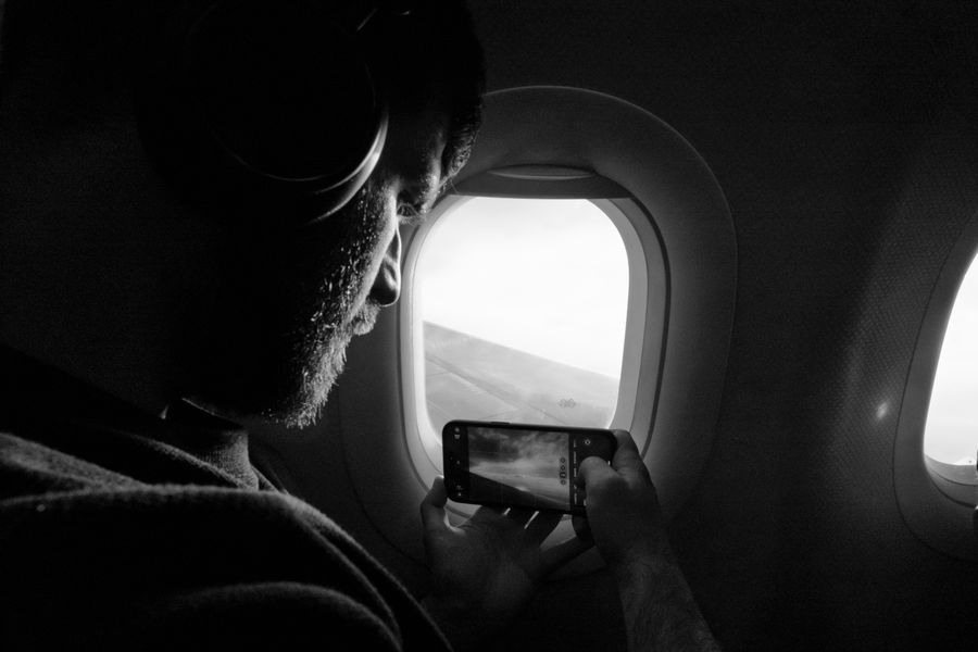 Man taking photo out of airplane window, capturing wing view with smartphone. — Carreteras costeras más allá de Argentina: el mapa sigue tu ritmo donde sea.