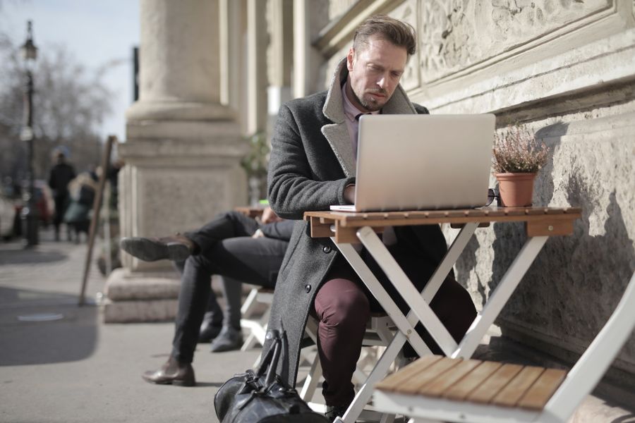 man in black jacket sitting on brown wooden folding chair using macbook — El casco antiguo de Dominican Republic: cada callejón mapeado, cada monumento identificado.