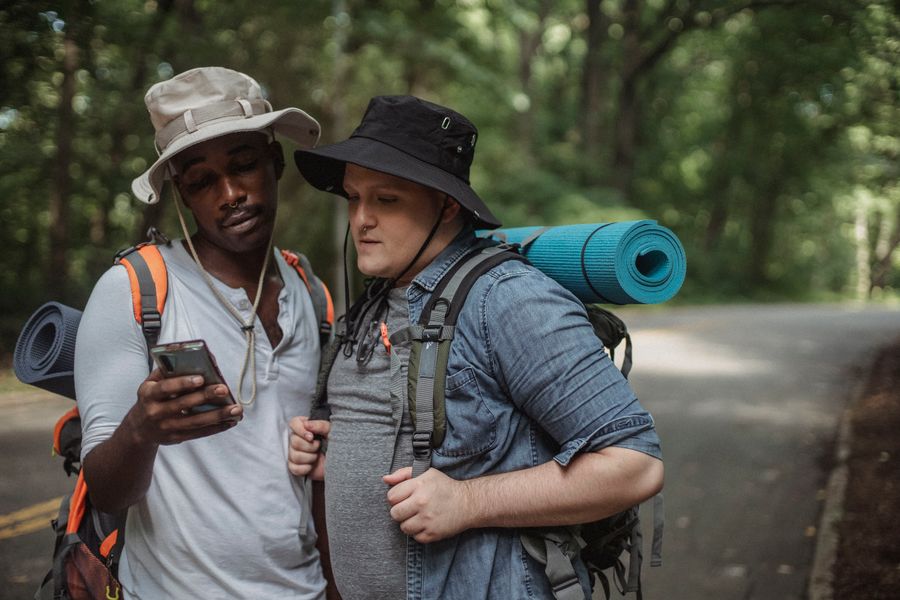 Young multiethnic tourists with hiking equipment surfing internet on cellphone on roadway against trees. — ¿Lluvia en Cuba? La conexión aguanta — el clima no limita los datos.