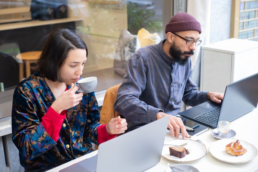 man and woman sitting in a cafe and using laptops while having a coffee and cake — El derby de Equatorial Guinea: boletos escaneados, repeticiones en streaming, viaje de vuelta reservado.