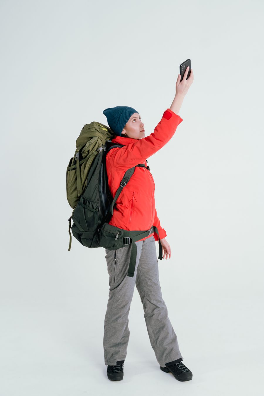 Young woman backpacker taking a selfie on a white background, dressed in outdoor gear. — El agente habla claro sobre cuándo esimgomobile NO es la respuesta.